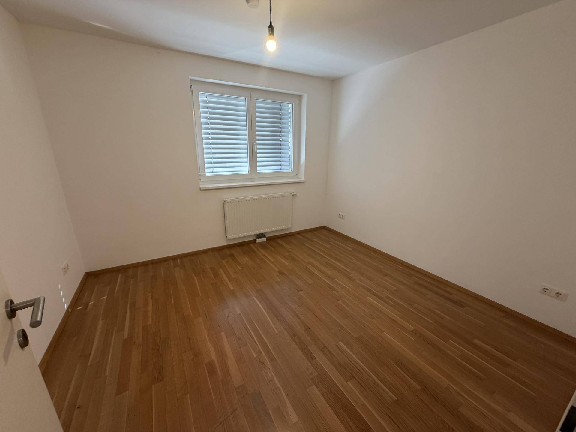 Leeres Schlafzimmer mit Parkettboden, Fenster und Heizkörper, bereit zur Einrichtung.