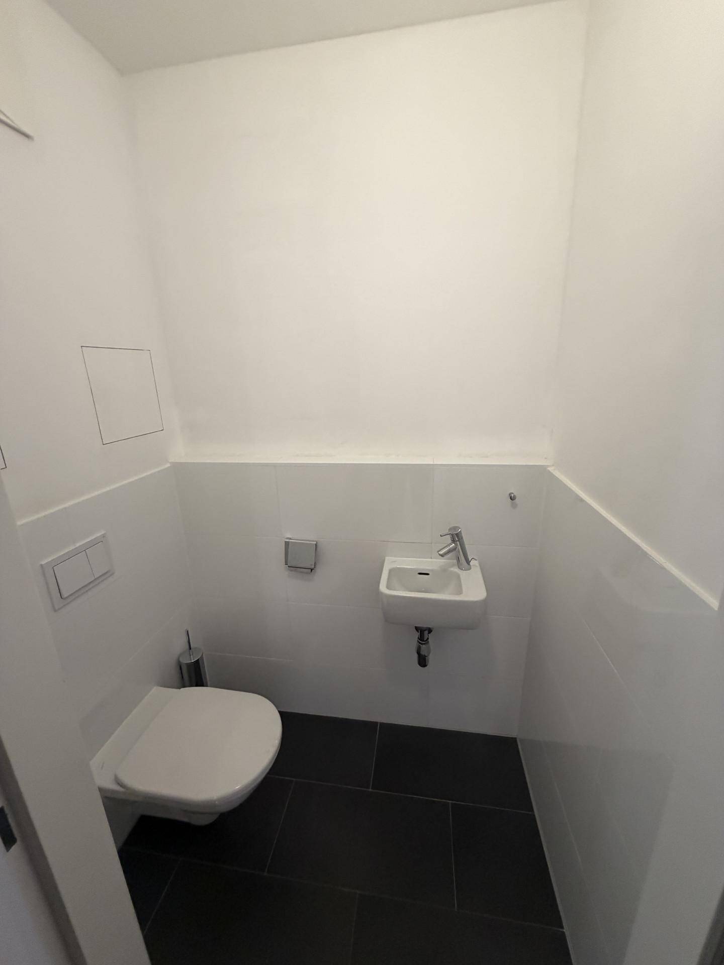Kleines Gäste-WC mit Wand-WC, Handwaschbecken und dunklen Bodenfliesen.