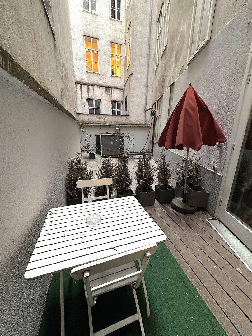 Kleiner Innenhof mit Tisch, Stühlen und Sonnenschirm, umgeben von hohen Mauern.