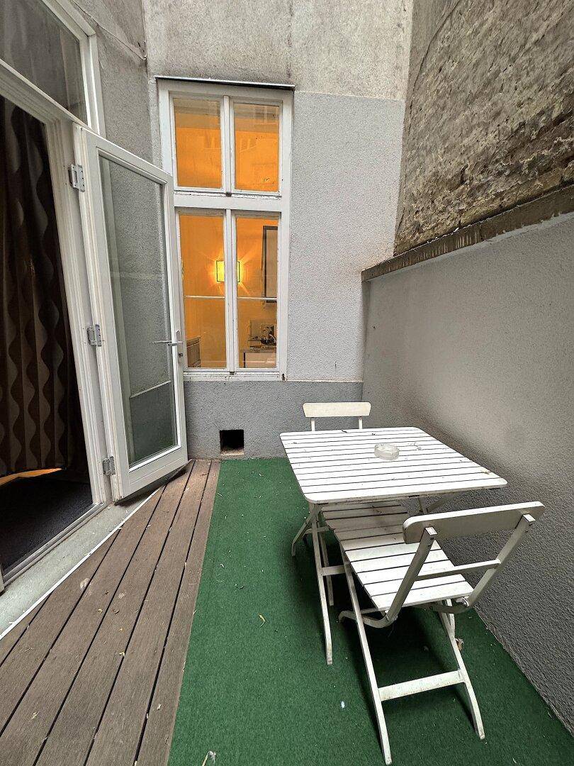 Gemütlicher Innenhof mit Sitzgelegenheiten und Zugang zum Gebäude durch eine Glastür.