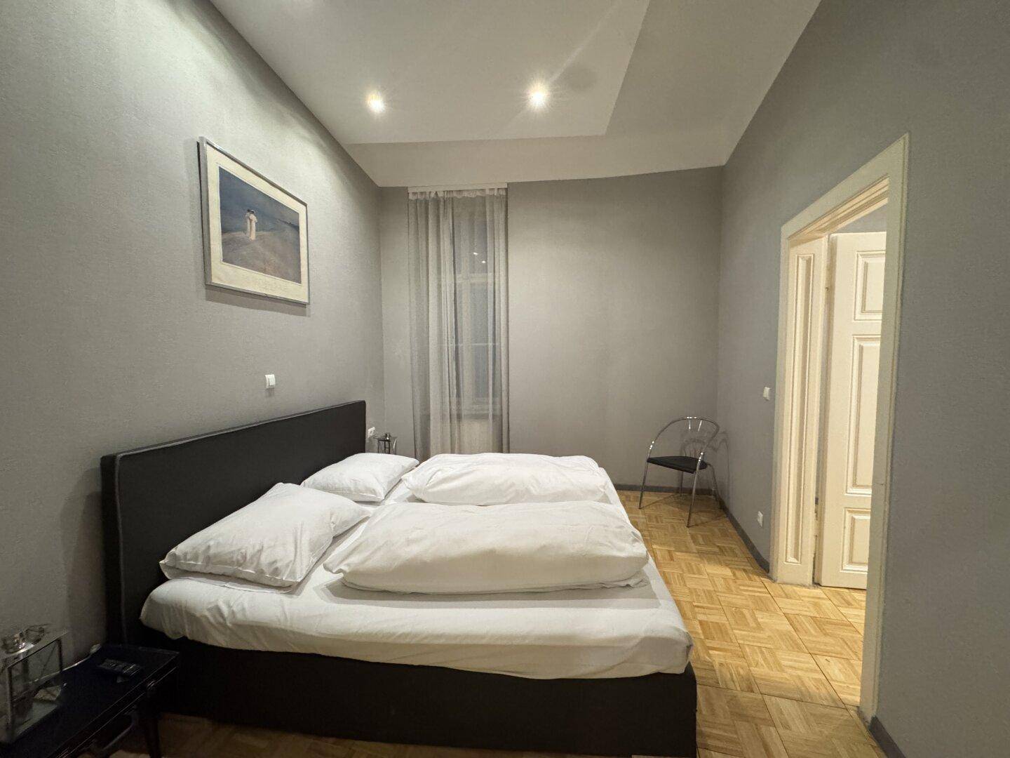 Gemütliches Schlafzimmer mit Doppelbett, Parkettboden und schlichten grauen Wänden.