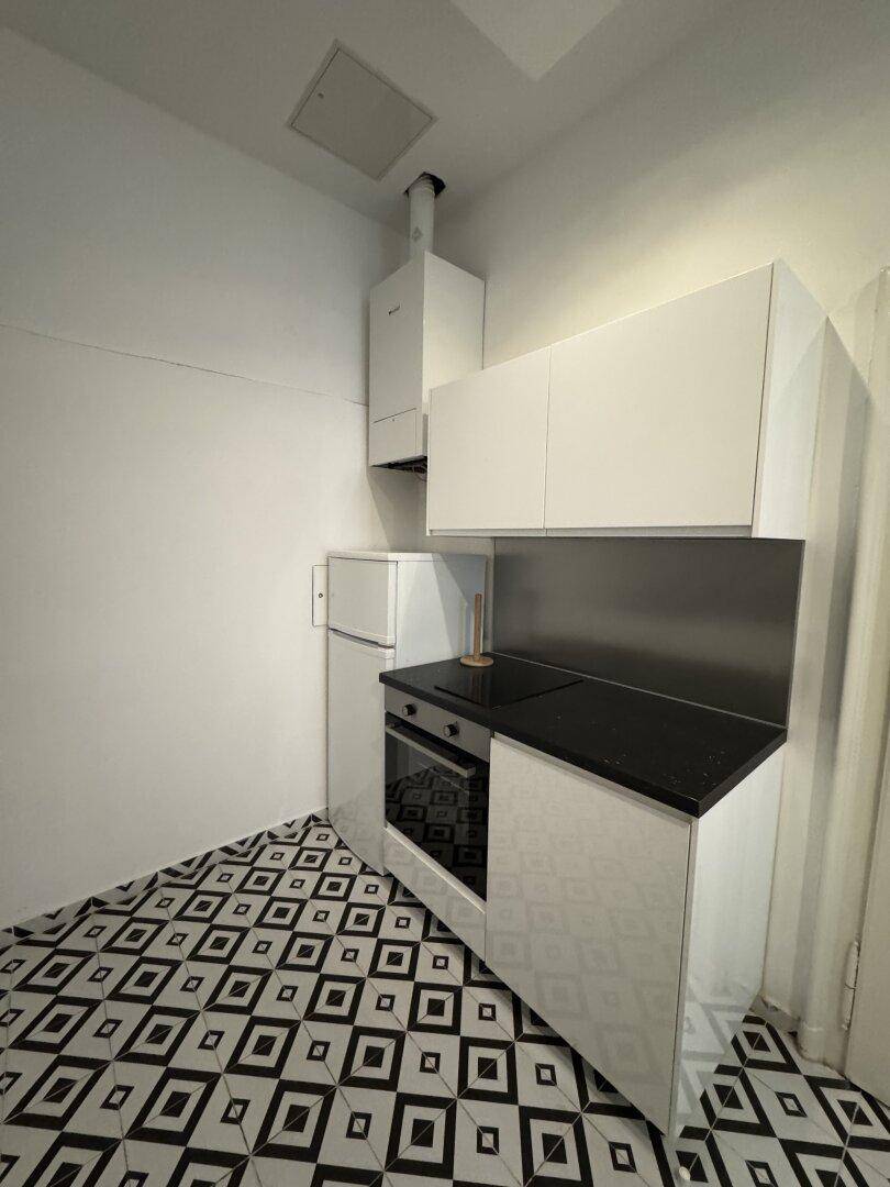 Küchenecke mit weißen Schränken, schwarzer Arbeitsplatte, Backofen und Kühlschrank.