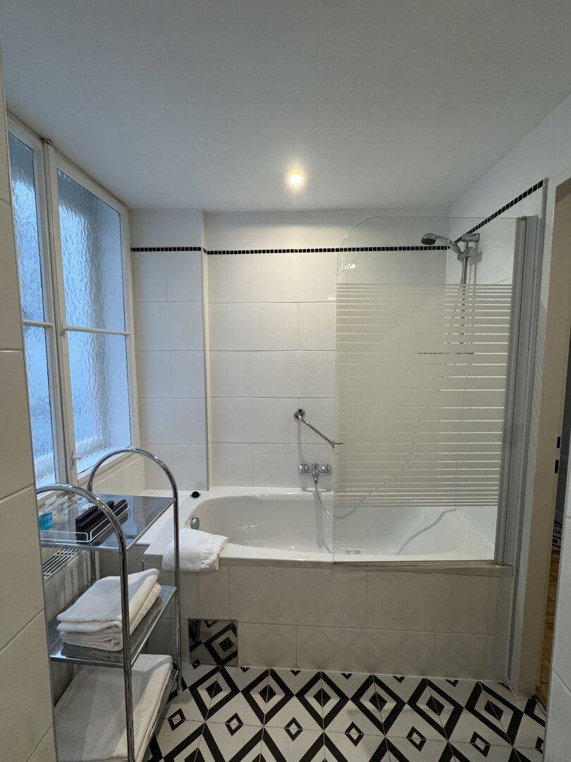 Badezimmer mit Badewanne, Duschabtrennung und auffälligen schwarz-weißen Fliesen.