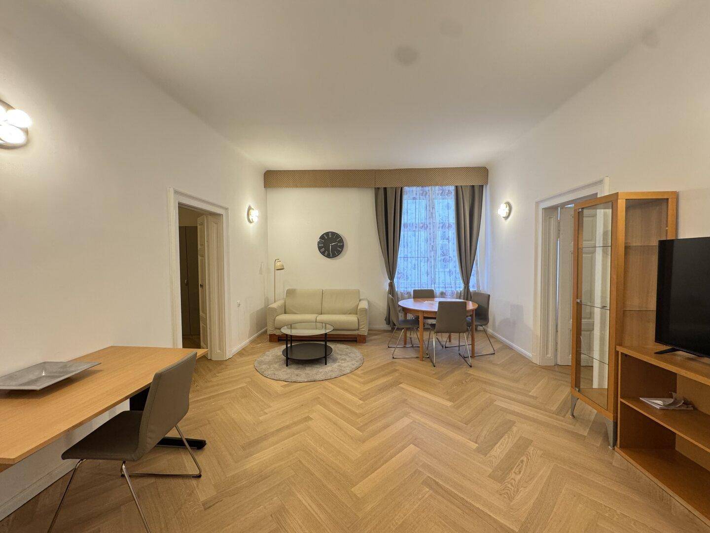 Geräumiger Wohn-Essbereich mit Fischgrätparkett, beigem Sofa und Esstisch.