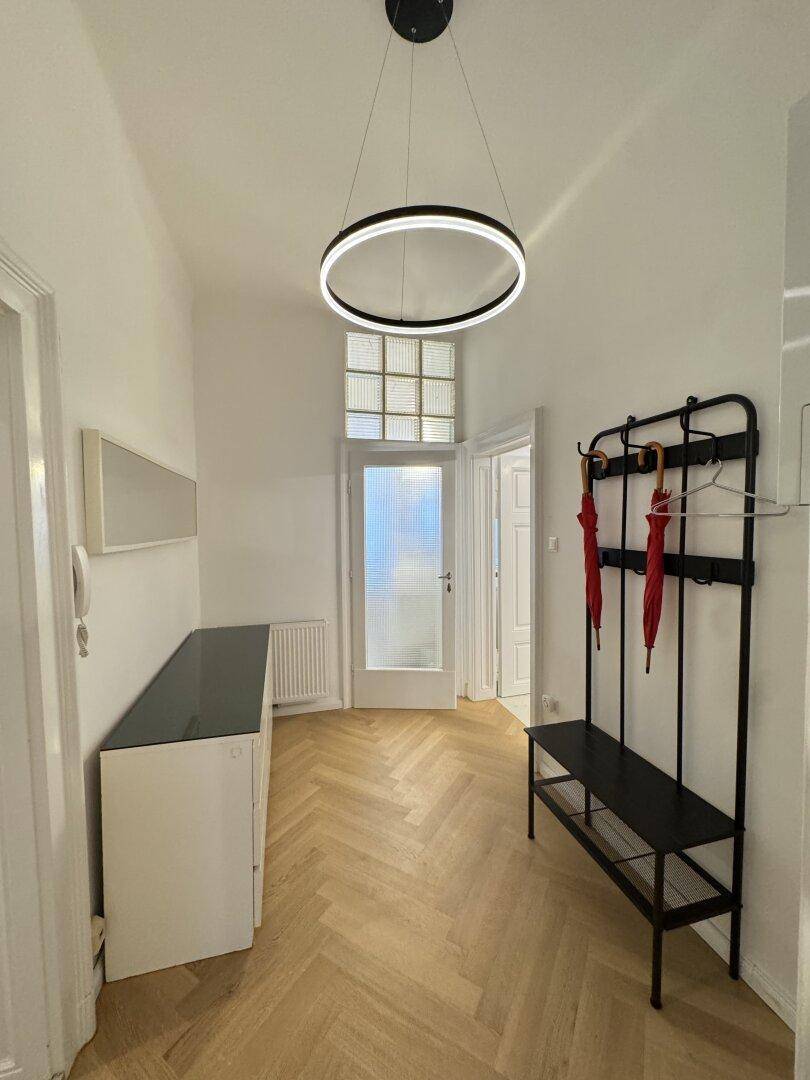 Heller Eingangsbereich mit modernem Lichtdesign, Fischgrätparkett und Garderobe.