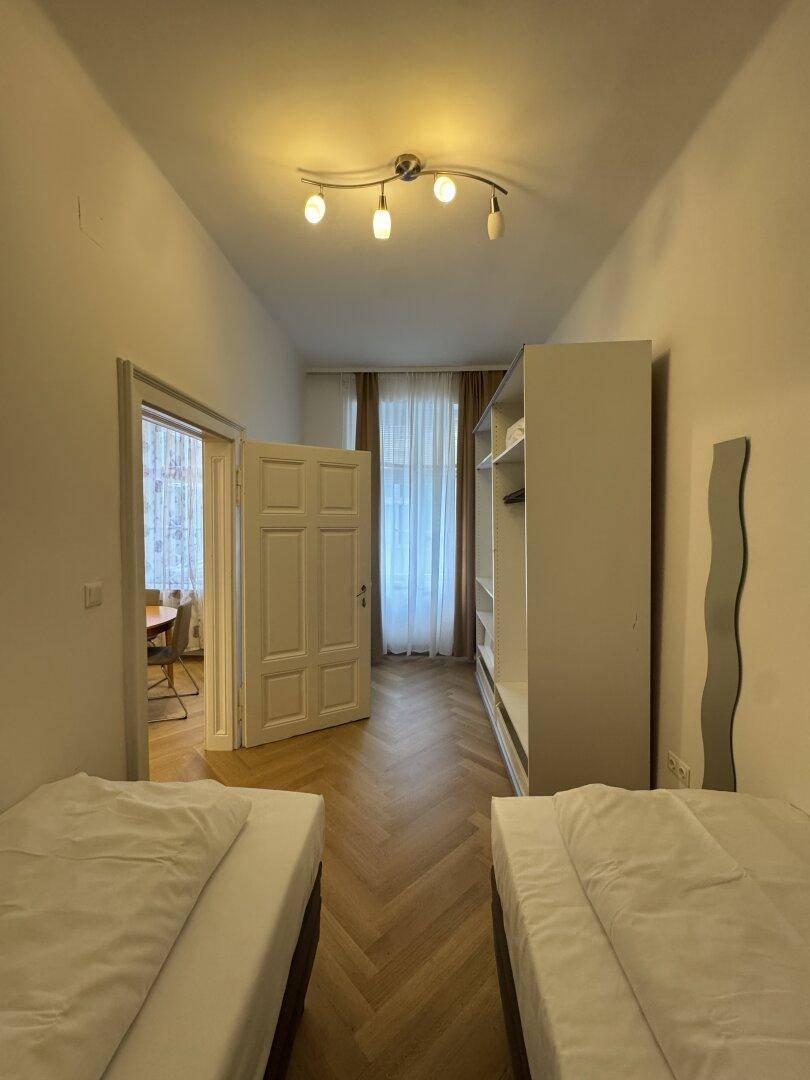 Schlafzimmer mit zwei Einzelbetten, Kleiderschrank und Fenster mit Vorhängen.