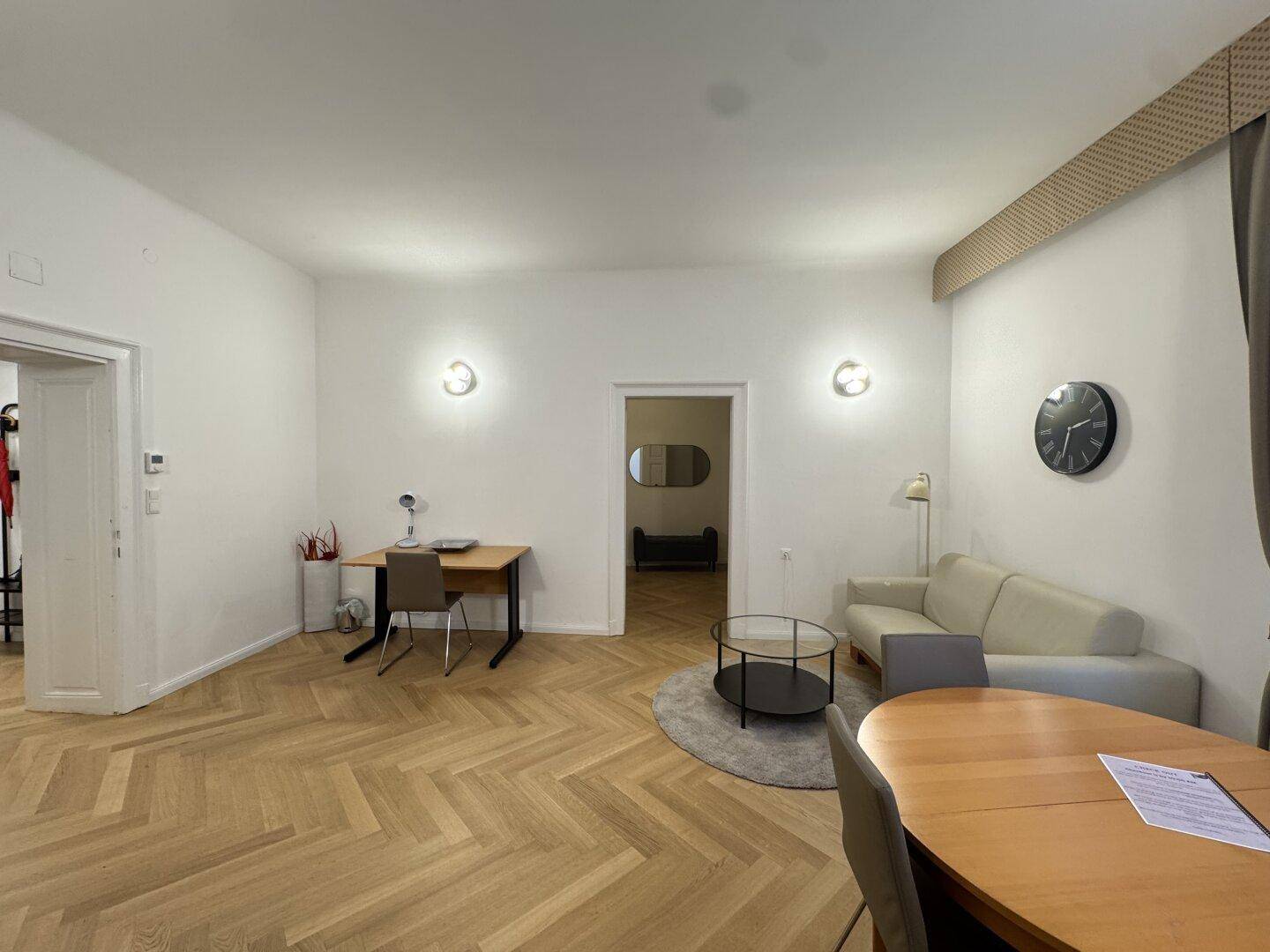 Großzügiger Wohn-Essbereich mit Arbeitsplatz, Sofa und Esstisch auf Fischgrätparkett.