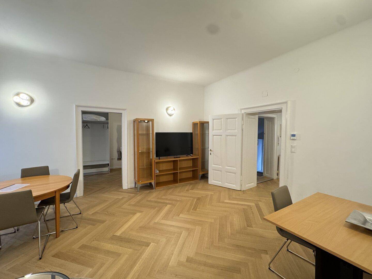 Wohn-Essbereich mit TV-Möbel, Esstisch und Zugang zu weiteren Räumen.