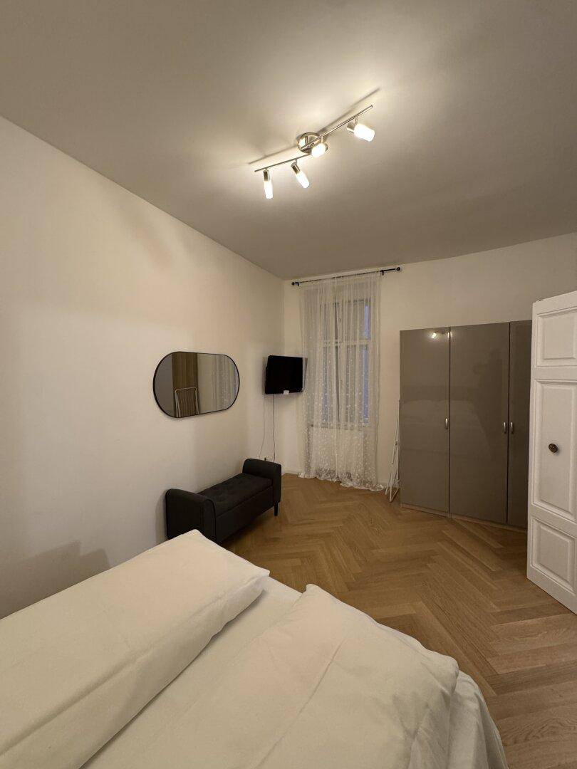 Schlafzimmer mit Doppelbett, modernem Kleiderschrank und Fenster mit Vorhängen.