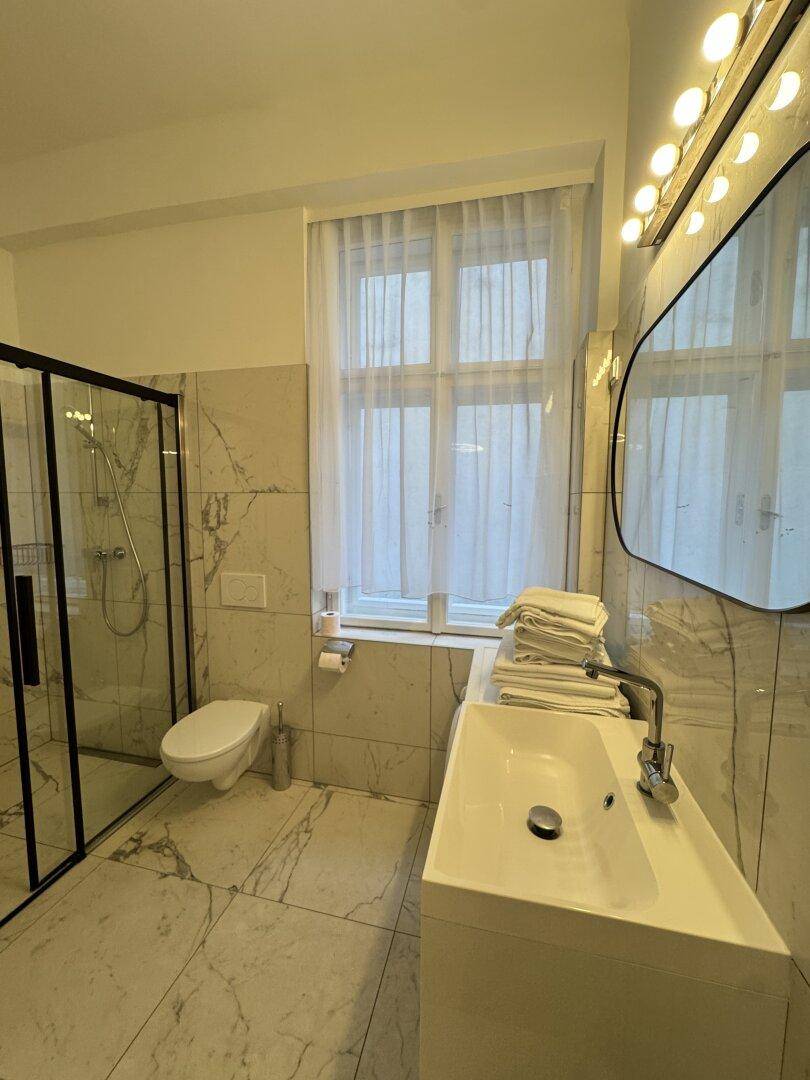 Modernes Badezimmer mit Marmorfliesen, Duschkabine, Waschbecken und Fenster.