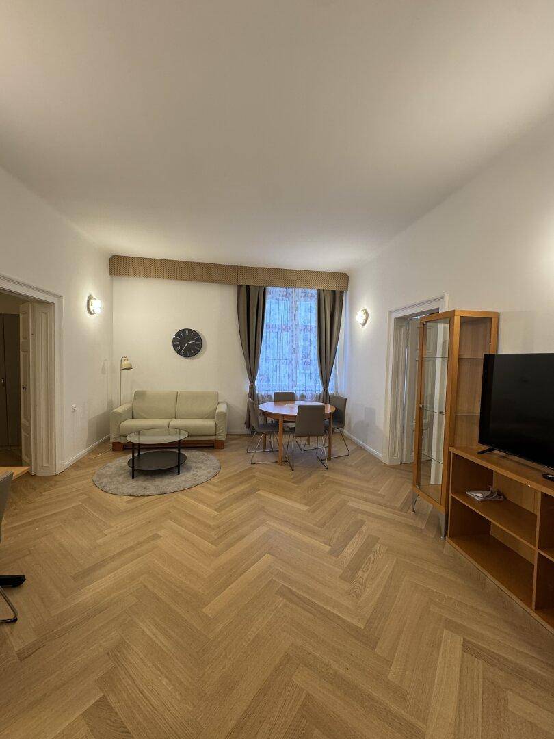 Heller Wohn-Essbereich mit Fischgrätparkett, beigem Sofa und Esstisch.