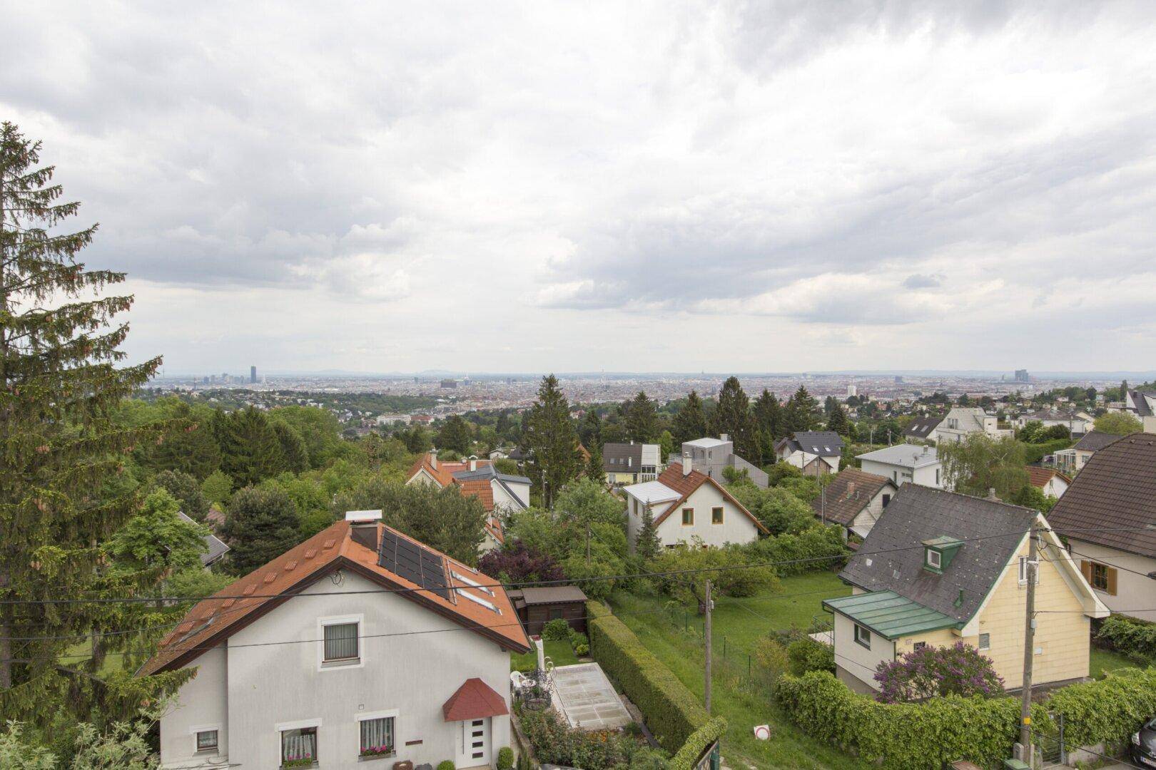 Weitläufiger Blick über die Stadt und die umliegende grüne Hügellandschaft unter bewölktem Himmel.