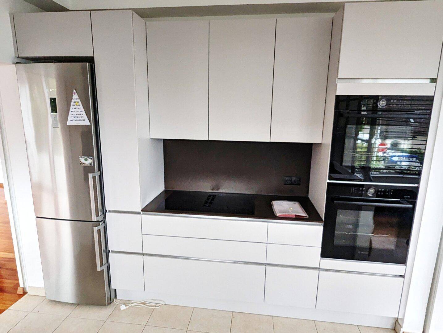 Moderne Einbauküche mit weißen Schränken, integrierten Geräten und Edelstahlkühlschrank.