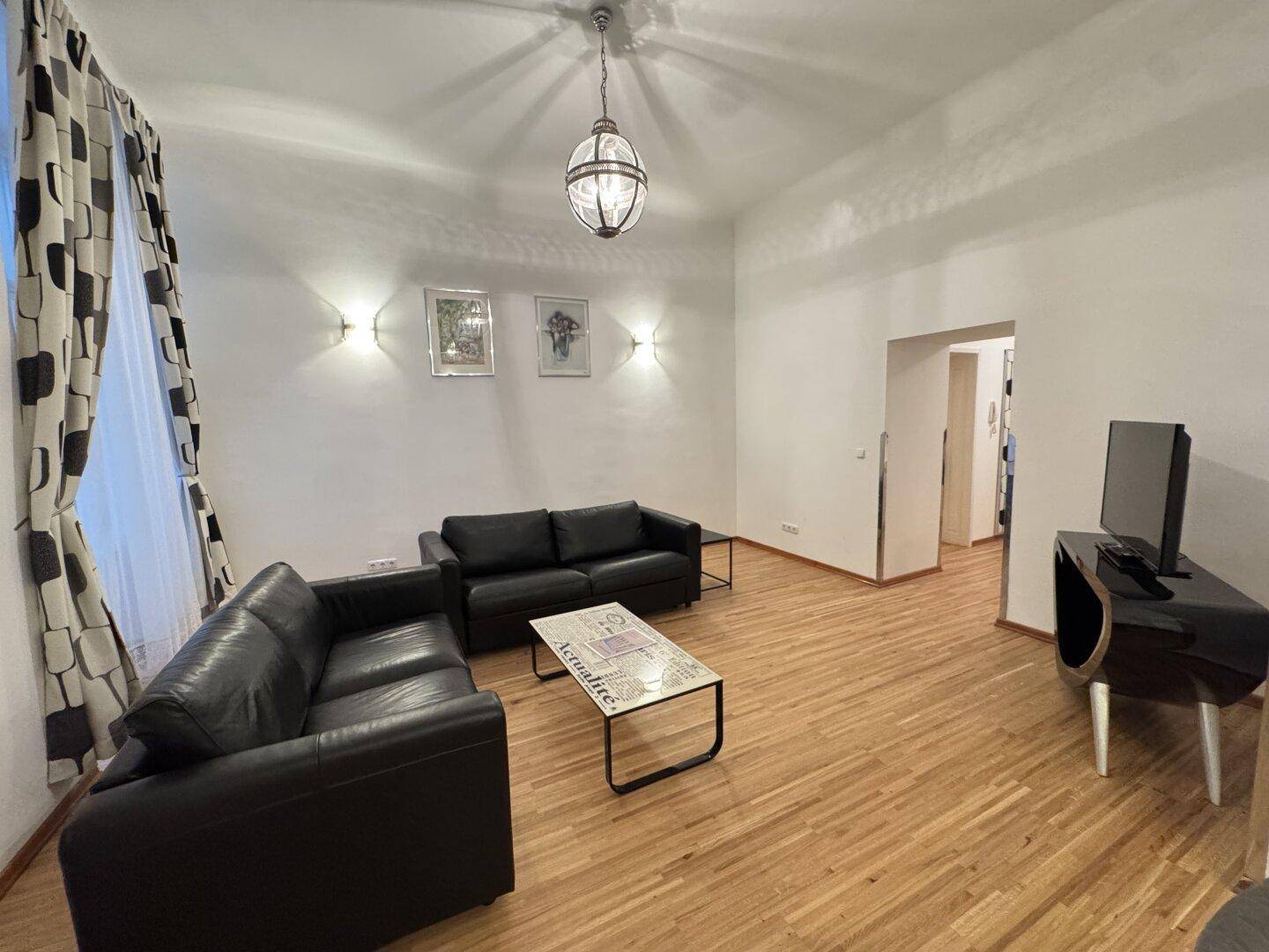 Geräumiges Wohnzimmer mit Holzparkett, zwei schwarzen Ledersofas und einem modernen Couchtisch.