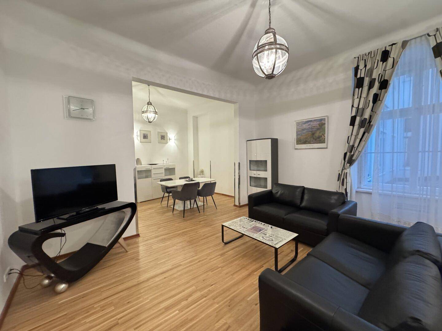 Heller Wohn- und Essbereich mit Holzparkett, schwarzen Sofas und einem Esstisch in modernem Stil.