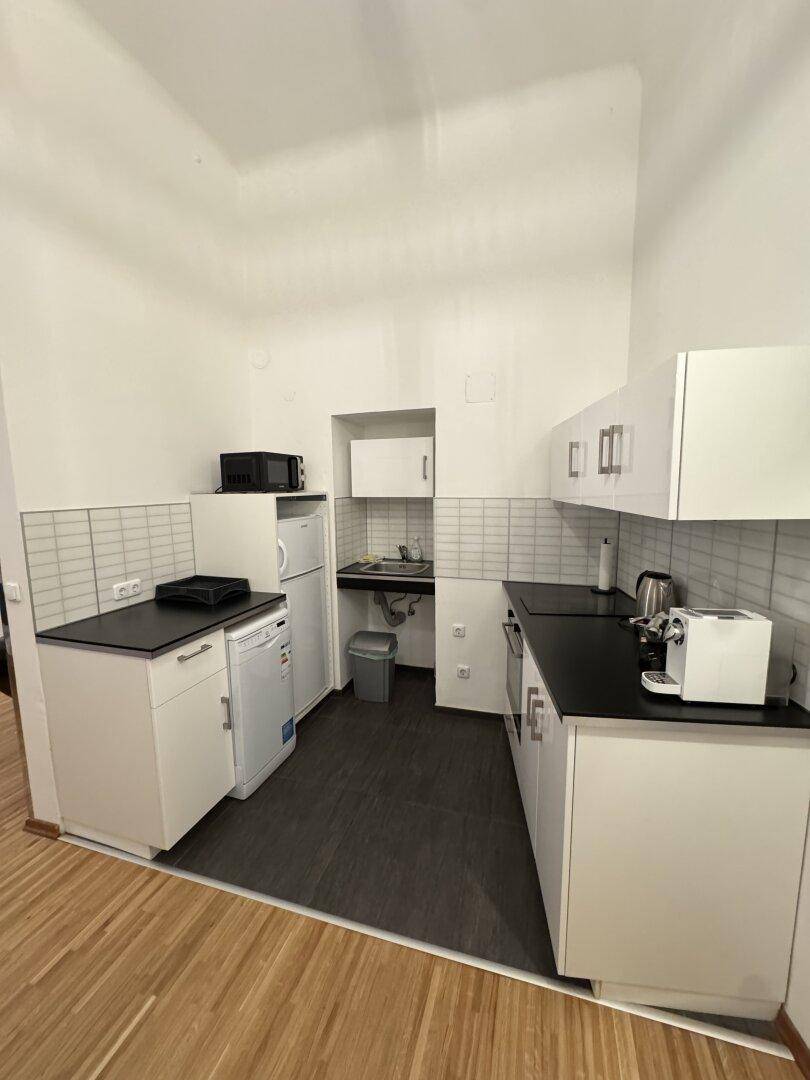 Kleine Küche mit weißen Schränken, dunklen Arbeitsplatten und Fliesen, ausgestattet mit Geräten.