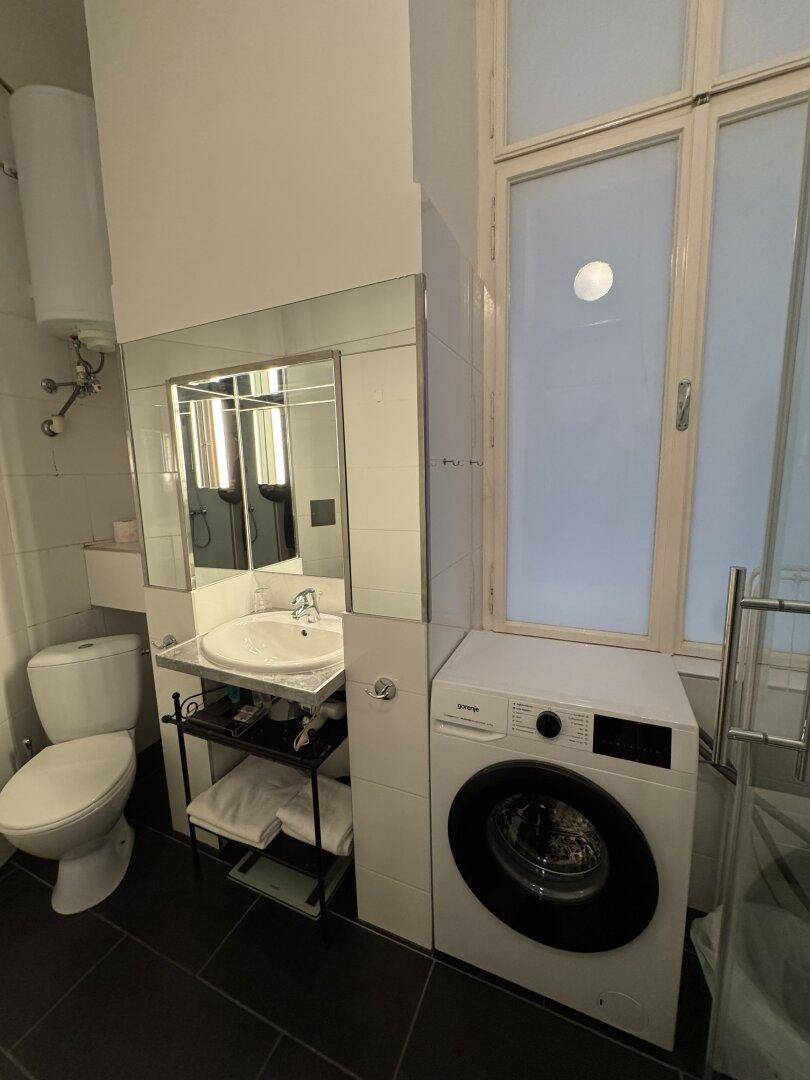 Badezimmer mit Waschbecken, Toilette, Waschmaschine und einem großen Fenster für natürliches Licht.