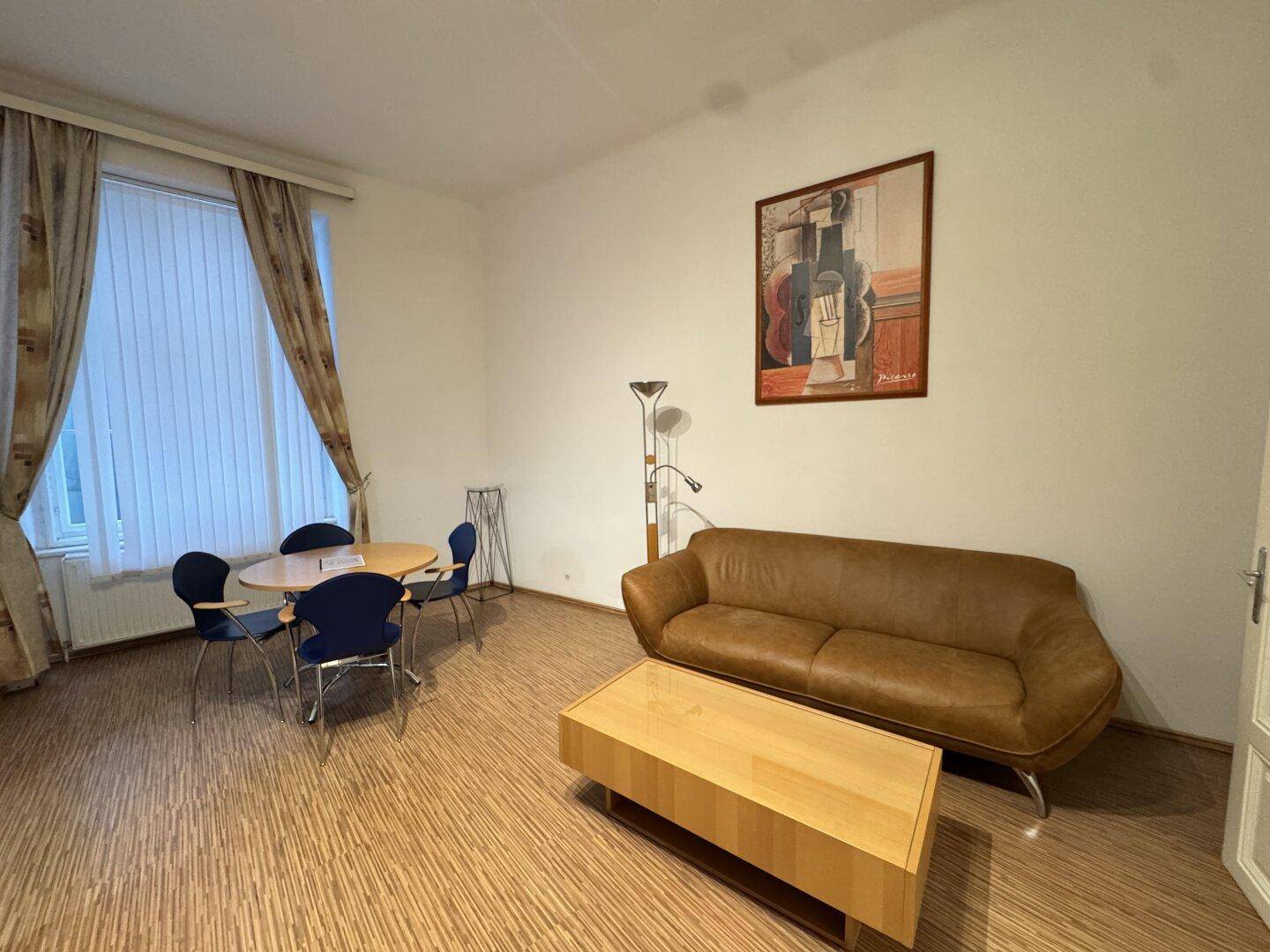 Wohn- und Essbereich mit bequemer Couch, Esstisch und einem Fenster mit Vorhängen.