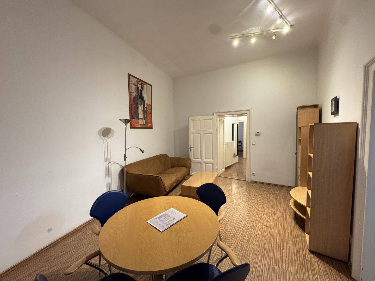 Wohnbereich mit Esstisch im Vordergrund, Couch und Regalsystem an der Wand.