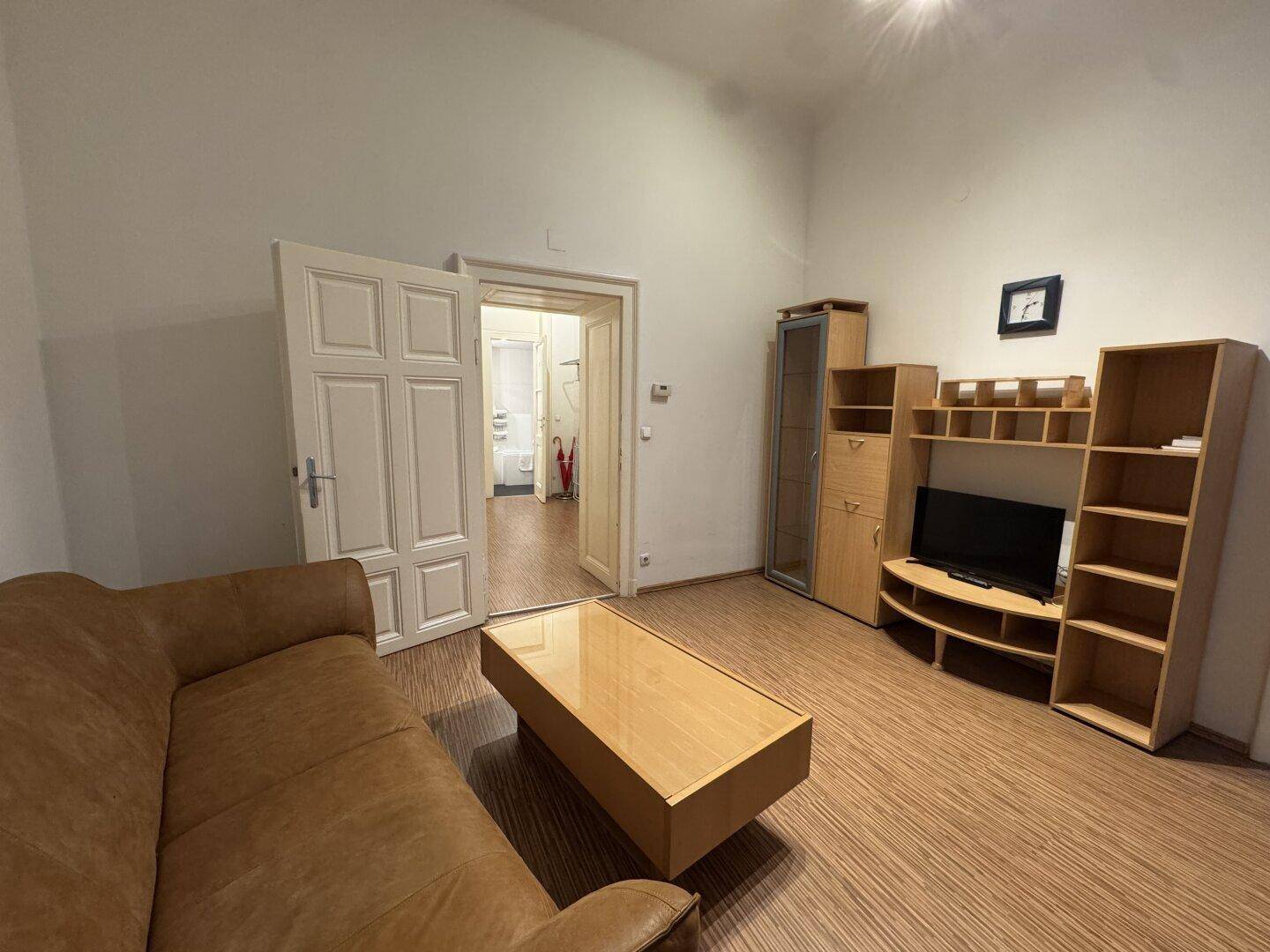 Wohnbereich mit Couch und Blick durch eine offene Tür in ein Badezimmer.