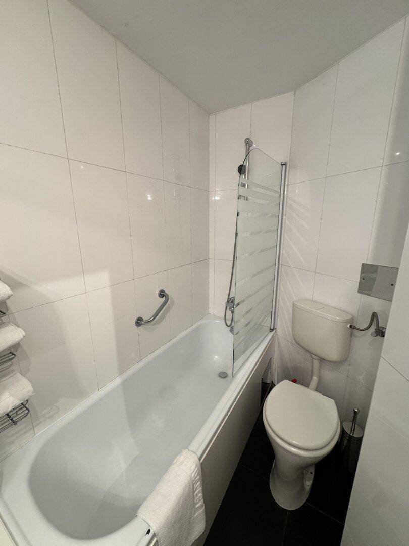 Badezimmer mit Badewanne, Duschabtrennung und weißen Fliesen an den Wänden.