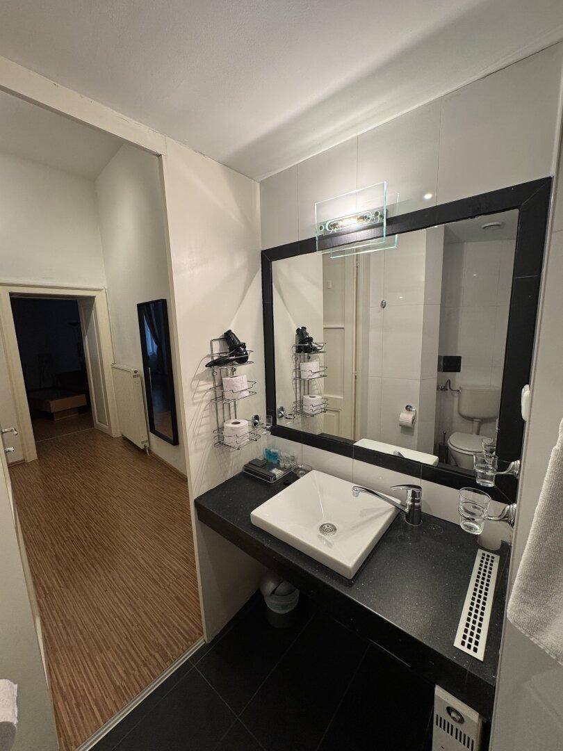 Badezimmer mit modernem Waschbecken, großem Spiegel und dunklen Bodenfliesen.