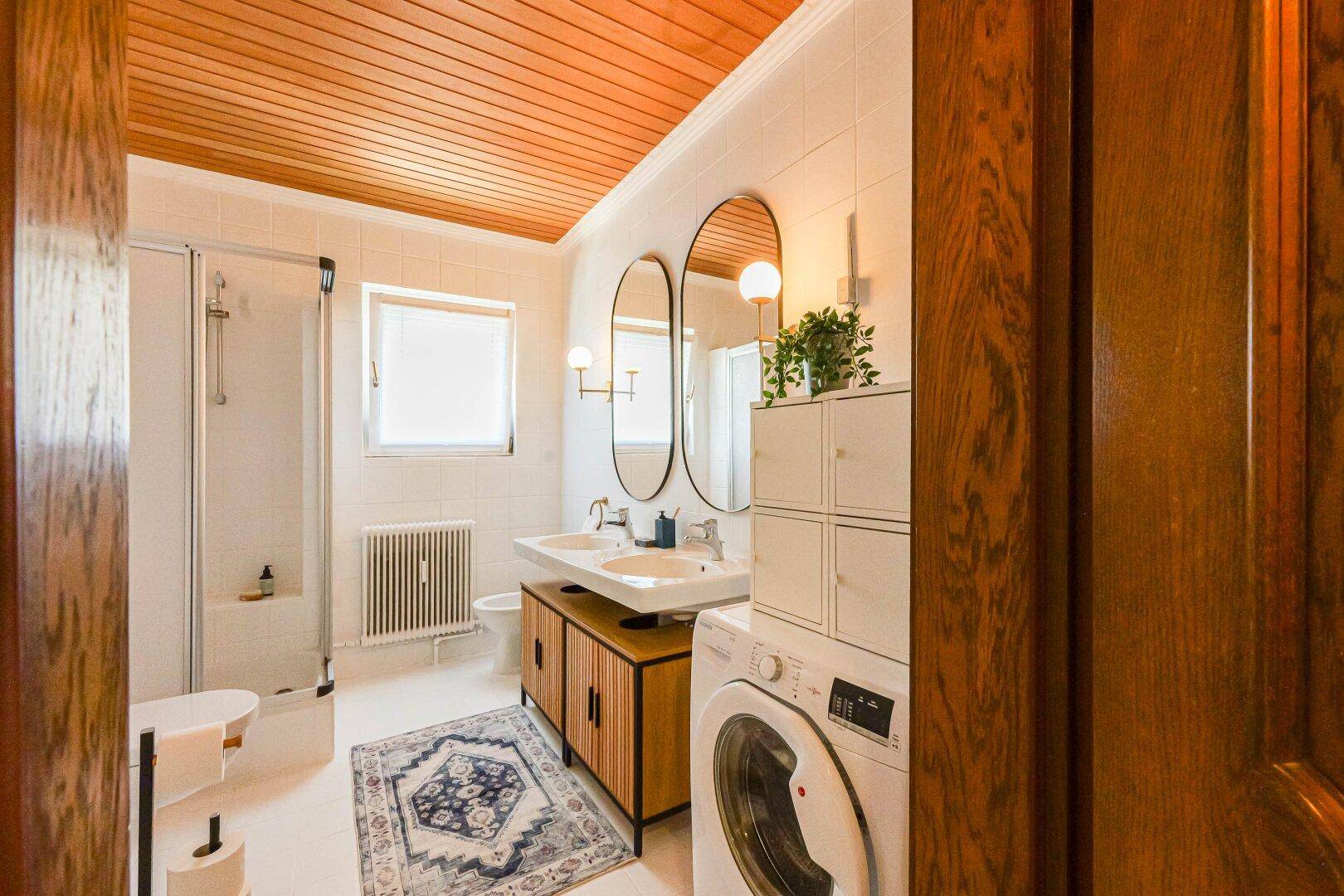 Modernes Badezimmer mit Doppelwaschbecken, Dusche und Holzdeckenverkleidung.