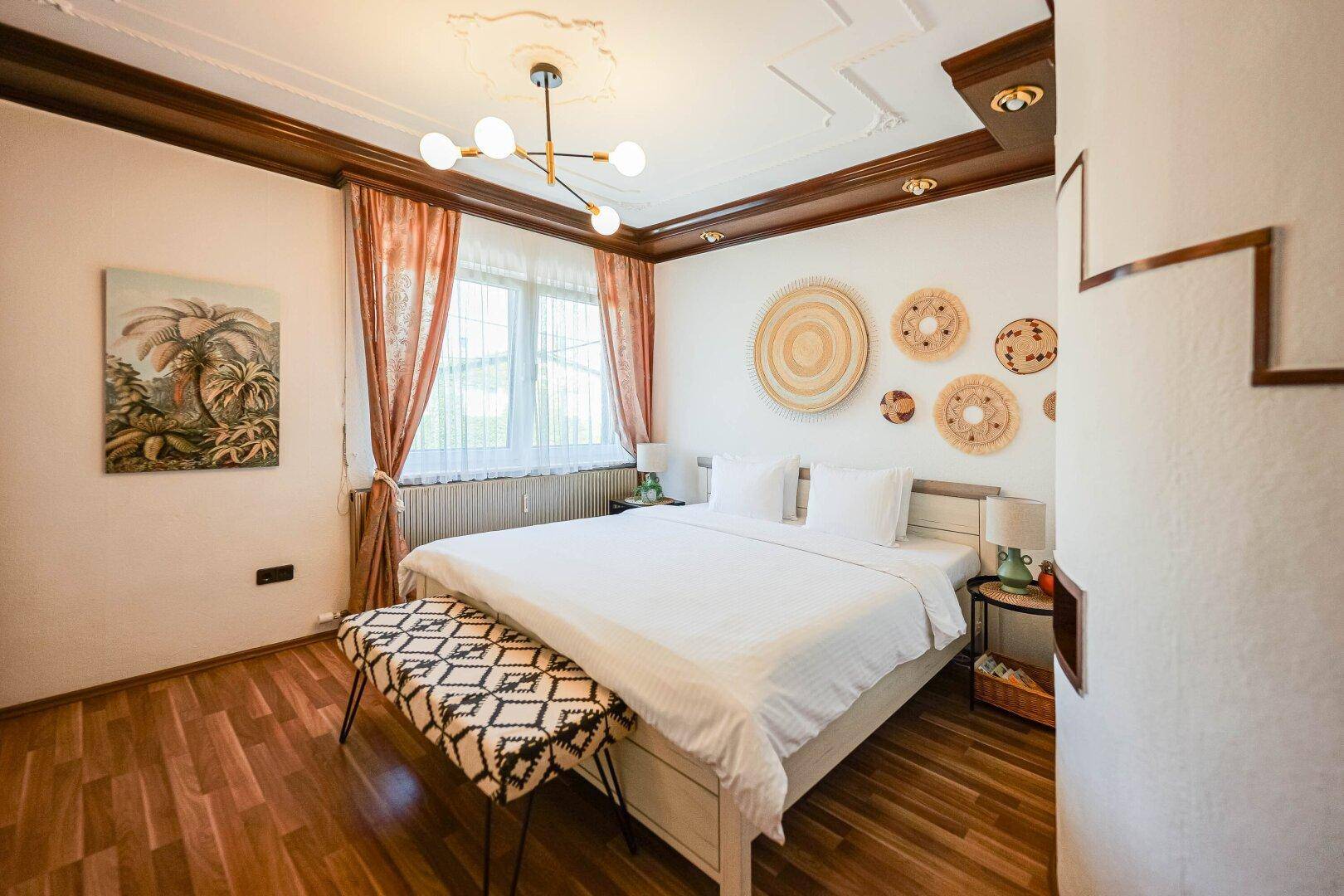 Gemütliches Schlafzimmer mit Holzboden, Doppelbett und dekorativer Deckenverzierung.