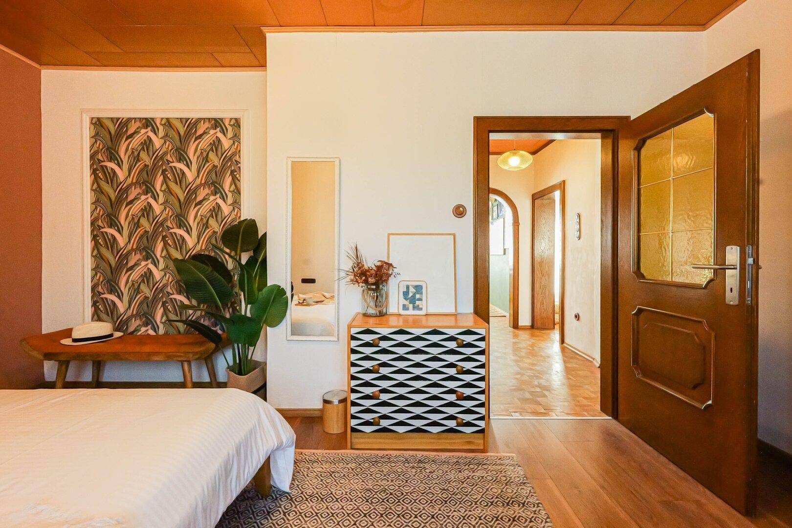 Schlafzimmer mit Holzboden, Kommode und Zugang zu einem weiteren Raum.