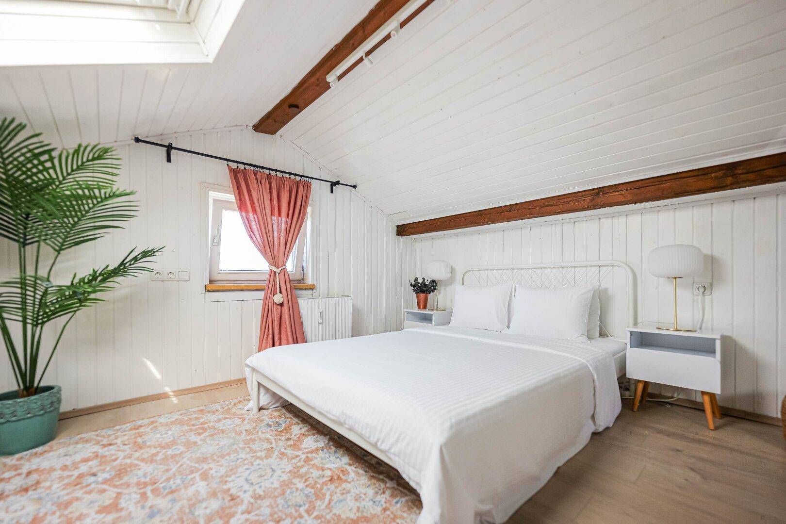 Helles Schlafzimmer im Dachgeschoss mit Dachfenster, Holzwänden und Holzbalken.