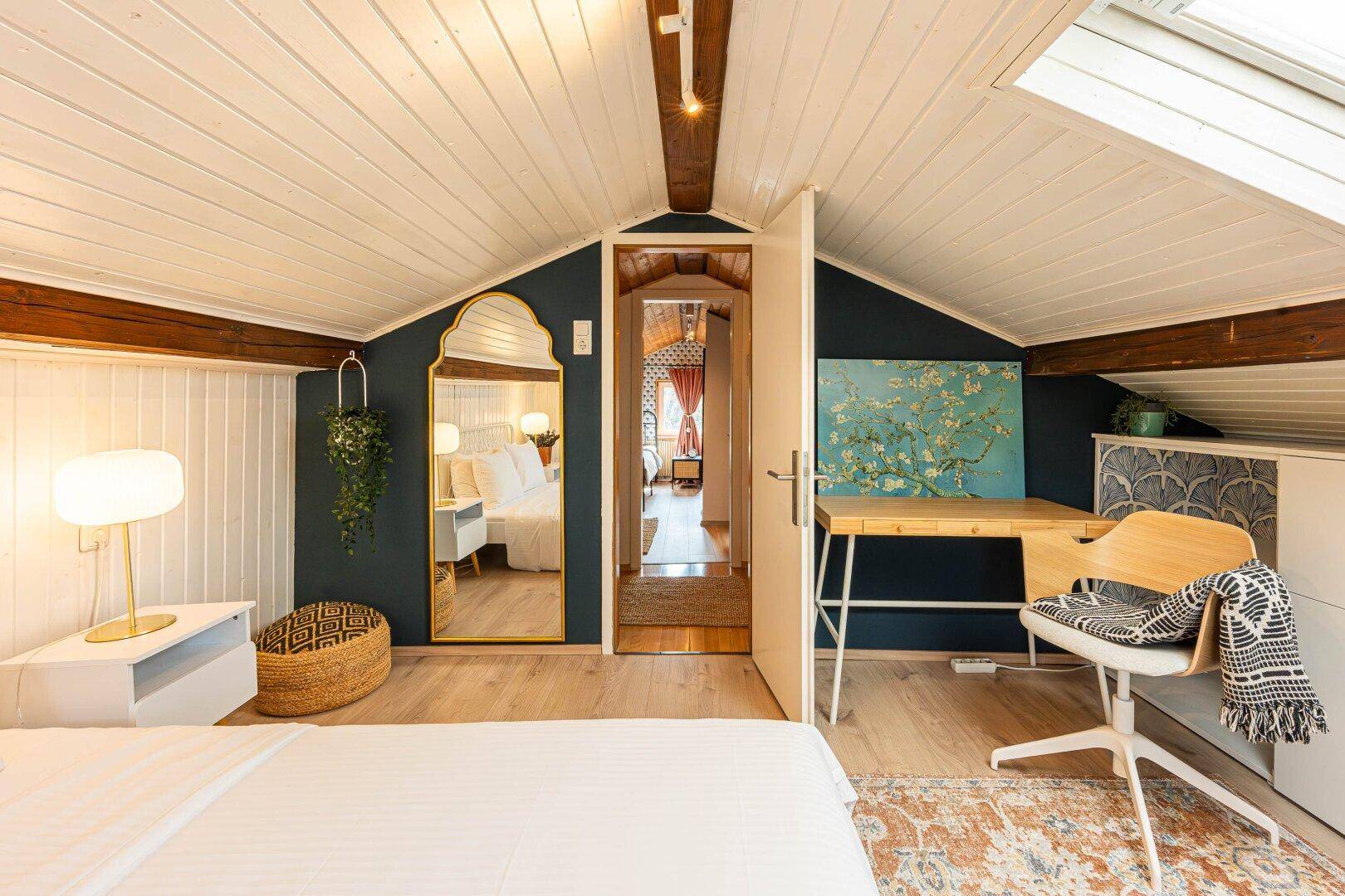 Dachgeschoss-Schlafzimmer mit Schreibtisch, Spiegel und Blick in den Flur.