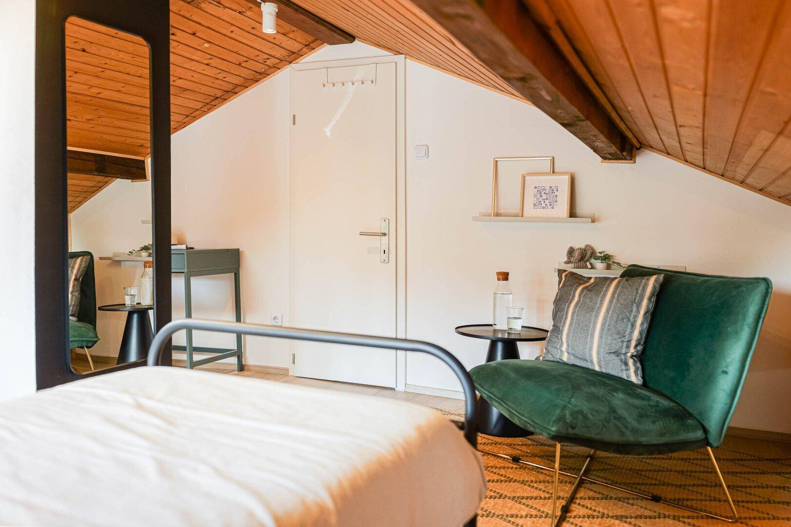 Dachgeschoss-Schlafzimmer mit Einzelbett, grünem Sessel und Spiegel.