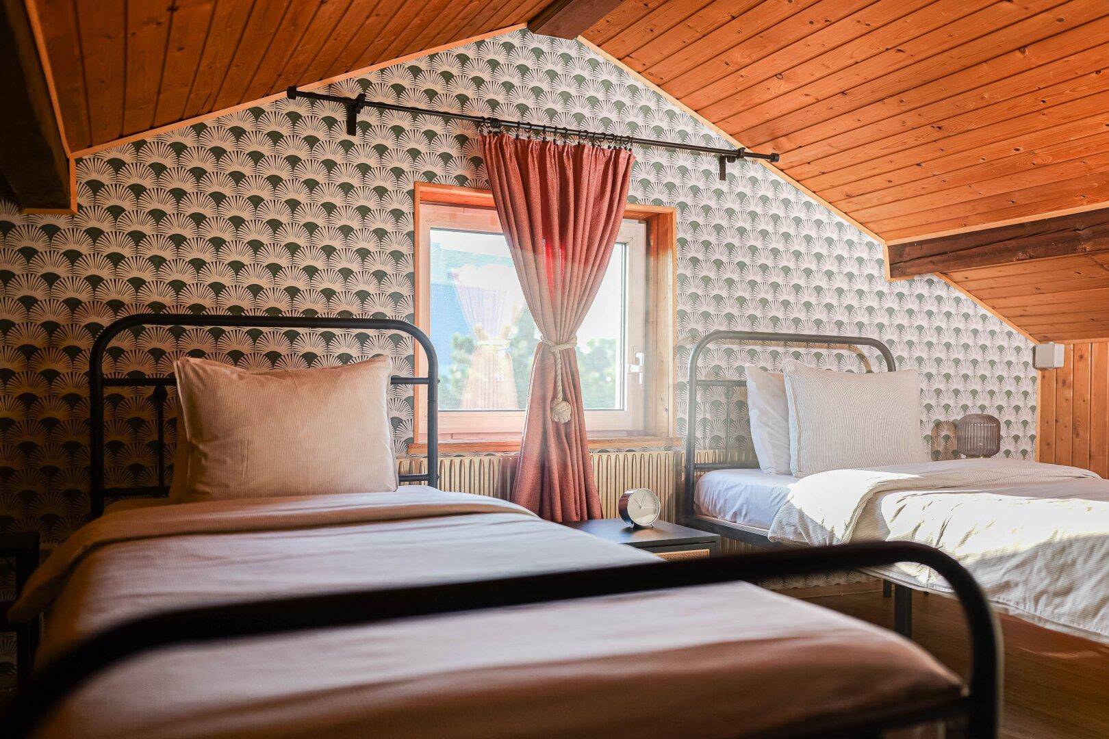 Dachgeschoss-Schlafzimmer mit zwei Einzelbetten, gemusterter Tapete und Holzdecke.