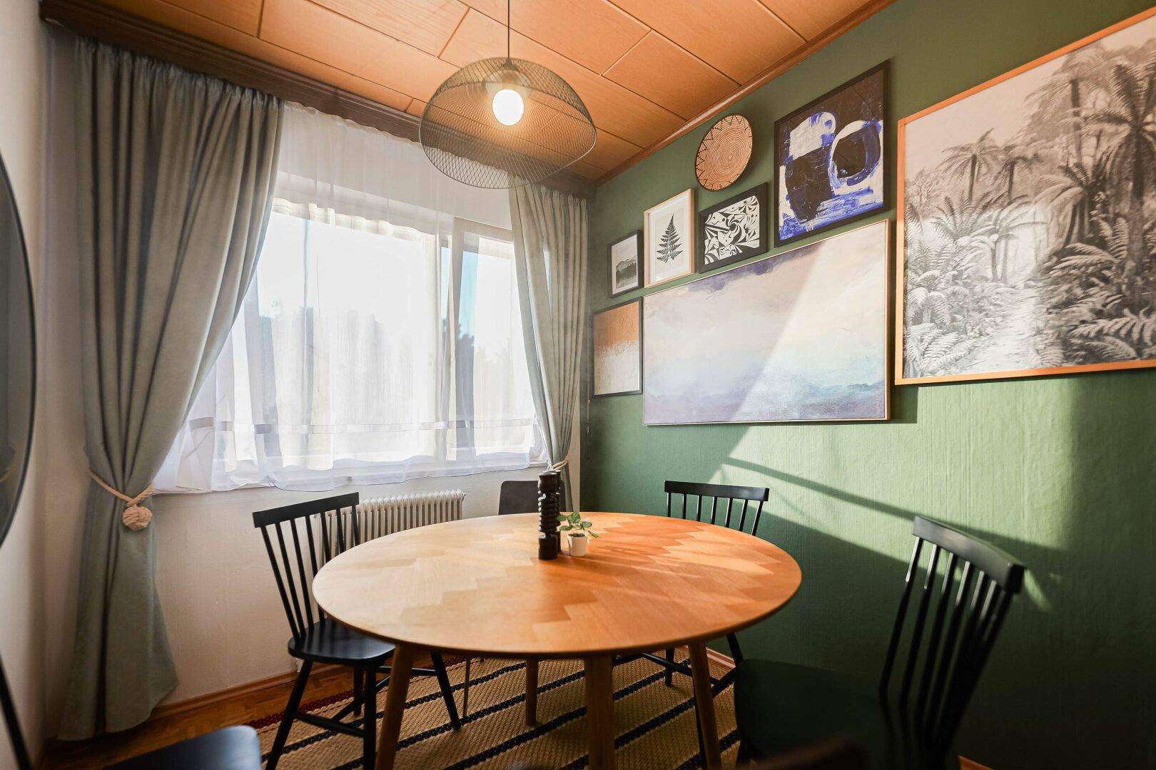 Esszimmer mit rundem Holztisch, grüner Wand und Kunstwerken.