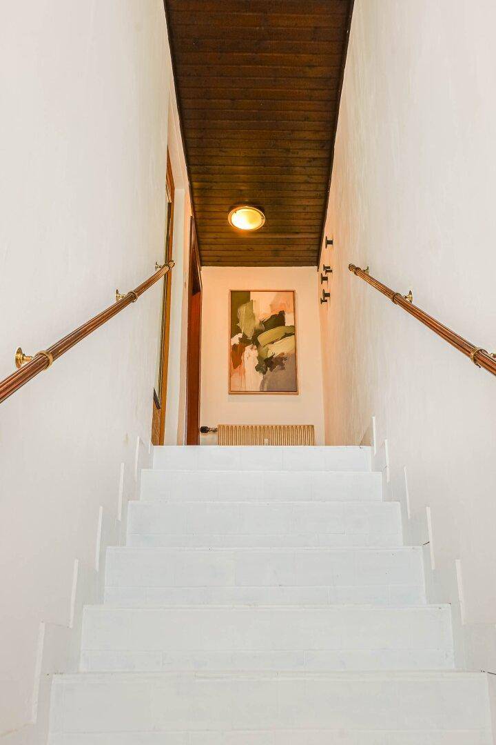 Treppenhaus mit weißen Stufen, Holzgeländer und Deckenverkleidung.