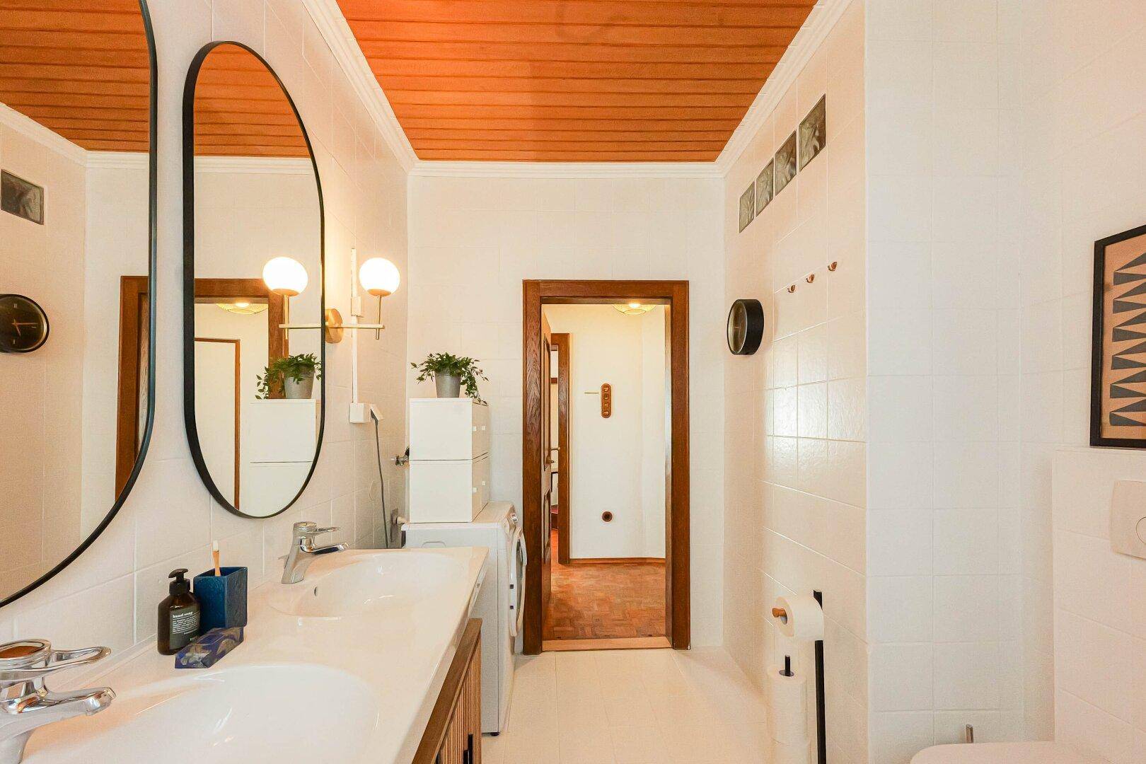 Helles Badezimmer mit Waschbecken, Spiegel und Holzdeckenverkleidung.
