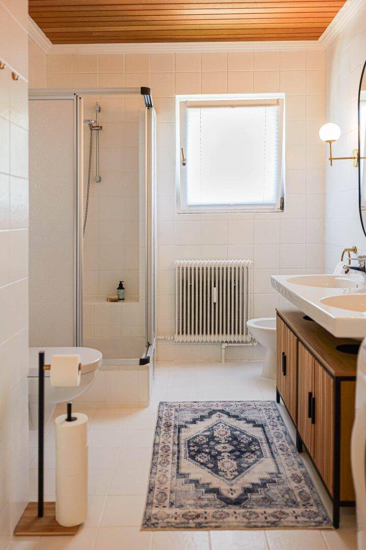 Helles Badezimmer mit Dusche, Doppelwaschbecken und Fenster.