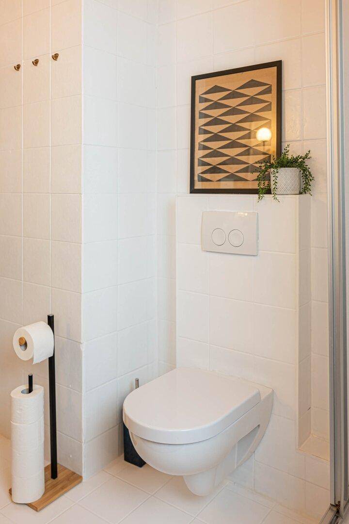 Modernes WC mit wandhängender Toilette und geometrischem Wandbild.