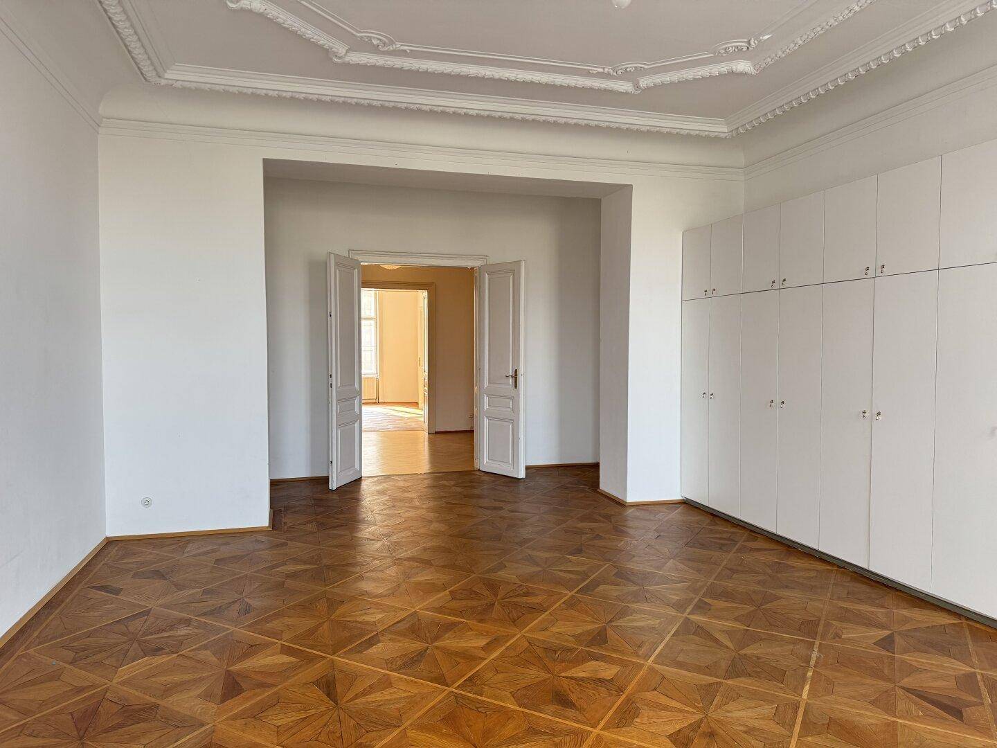Helles Wohnzimmer mit Fischgrätparkett, hohen Decken und integrierten Wandschränken.