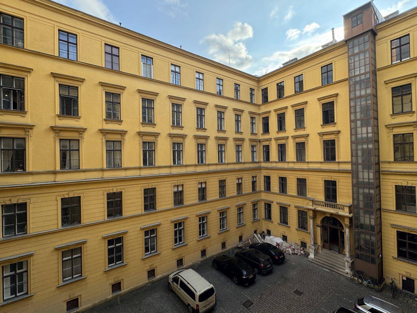 Innenhof eines historischen Gebäudes mit Parkplätzen und einem externen Aufzug.