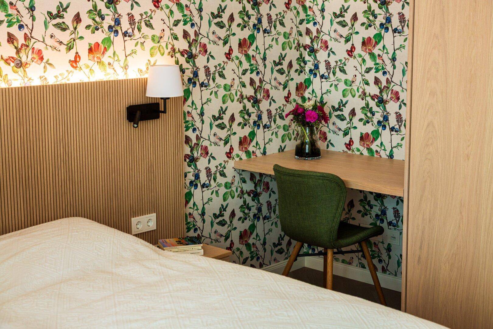 Schlafzimmer mit floraler Tapete, Holzakzenten und einem praktischen Schreibtischbereich.