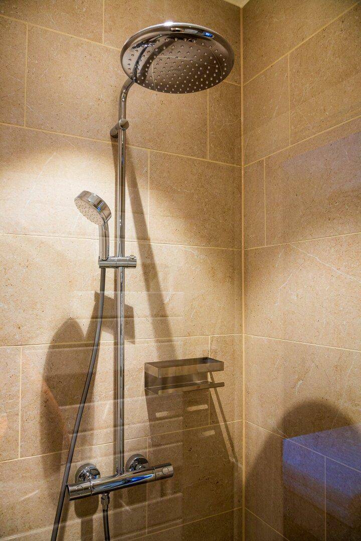 Moderne Dusche mit Regenduschkopf und Handbrause in einem gefliesten Badezimmer.