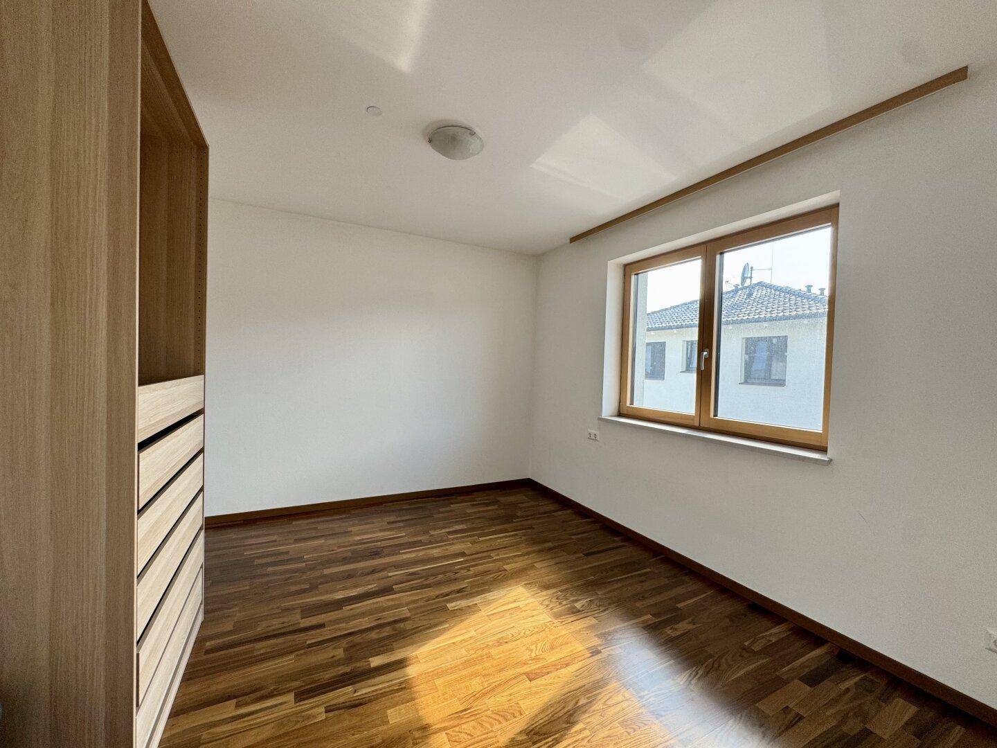 Helles Schlafzimmer mit Holzboden, weiß gestrichenen Wänden und einem großen Fenster.