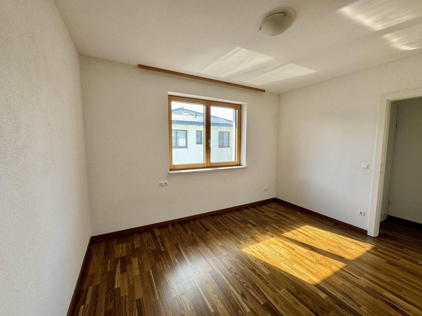 Geräumiges Schlafzimmer mit Holzboden und viel Tageslicht durch das große Fenster.