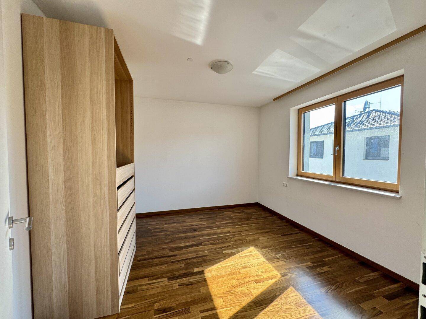 Freundliches Schlafzimmer mit Holzboden, weiß gestrichenen Wänden und einem Einbauschrank.