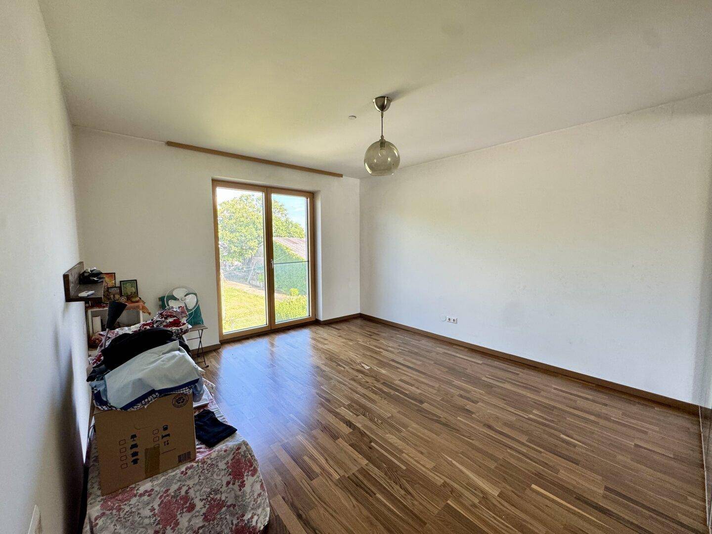 Geräumiges Zimmer mit Holzboden und viel Tageslicht durch die große Terrassentür.
