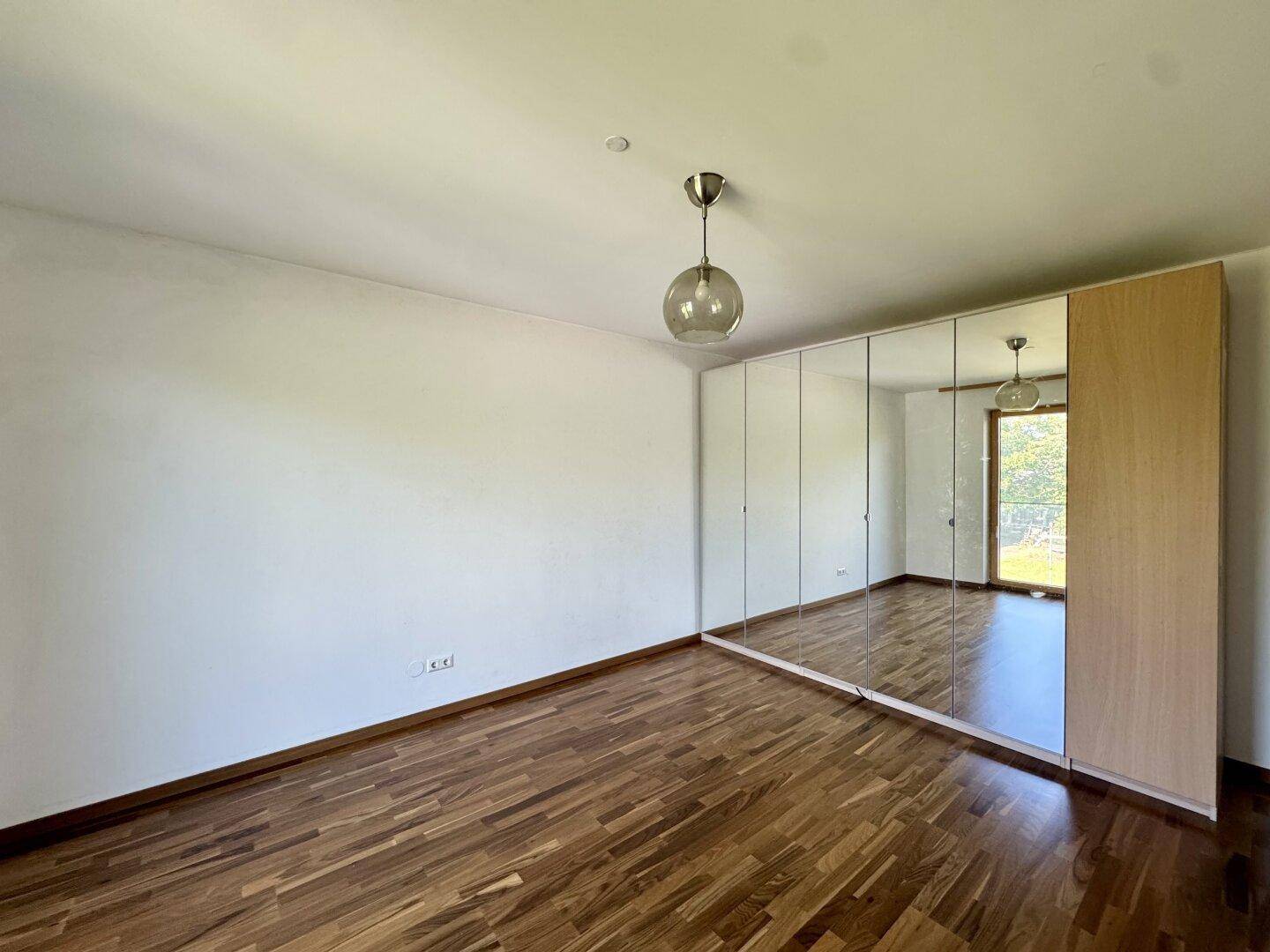 Helles Zimmer mit Holzboden und einem großen Spiegelschrank, der den Raum optisch vergrößert.