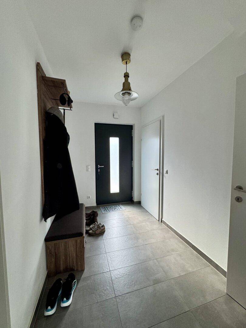 Heller Eingangsbereich mit Fliesenboden, Garderobe und moderner Haustür.