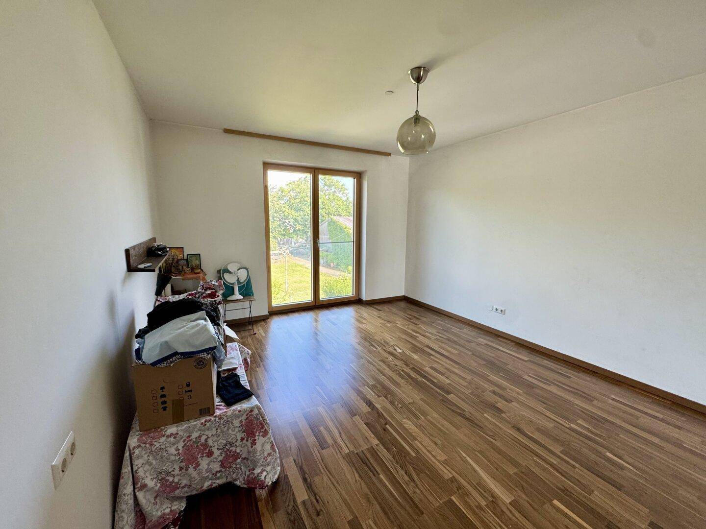 Geräumiges Zimmer mit Holzboden und viel Tageslicht durch die große Terrassentür.