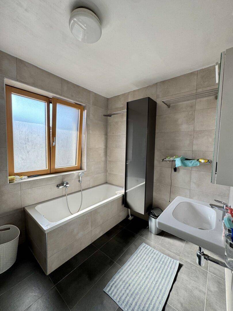 Modernes Badezimmer mit Badewanne, Waschbecken und einem Fenster für natürliche Belüftung.
